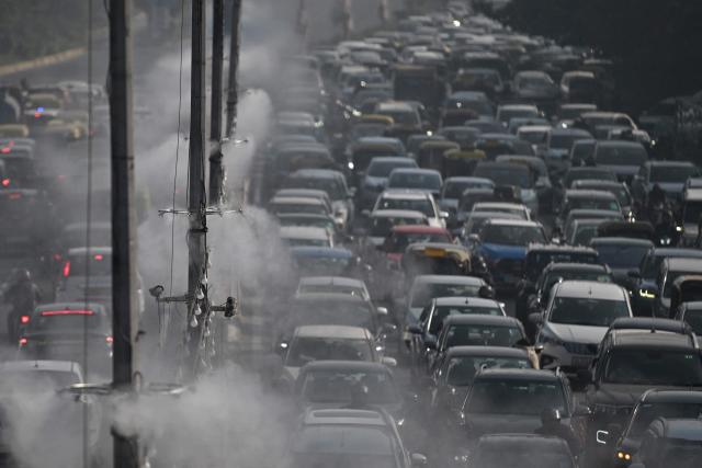 Commuters drive past as anti-smog sprinklers on lamp posts spray water to curb air pollution in New Delhi on December 9, 2025. (Photo by Arun SANKAR / AFP)