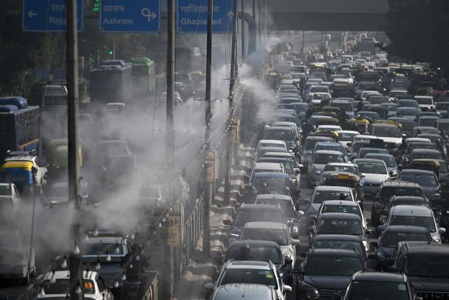 Commuters drive past as anti-smog sprinklers on lamp posts spray water to curb air pollution in New Delhi on December 9, 2025. (Photo by Arun SANKAR / AFP)