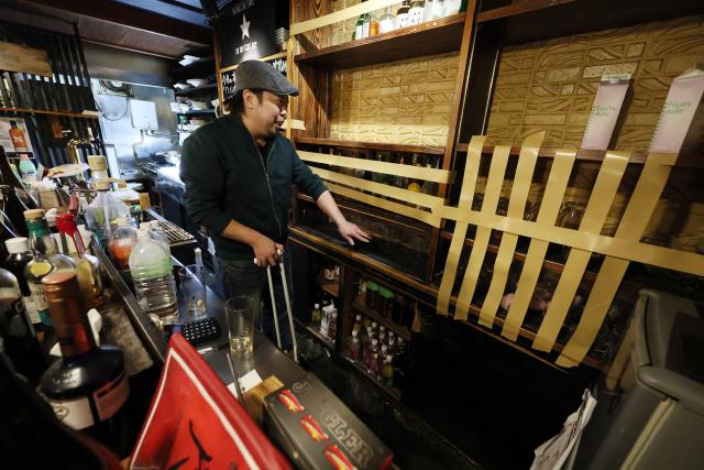An employee uses adhesive tape to reinforce bottles and glasses to prevent them from falling at a pub where dishes and other items were scattered due to an earthquake in Hachinohe City, Aomori Prefecture on December 9, 2025. A big quake off northern Japan left at least 30 injured, authorities said on December 9, damaging roads and leaving thousands without power in freezing temperatures. (Photo by JIJI Press / AFP) / Japan OUT