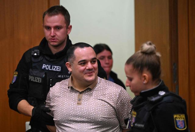 Co-defendant Ukrainian Robert A., is lead into the courtroom on the opening day of the trial of three men on charges of spying for Russia, in Frankfurt am Main, western Germany, on December 9, 2025. Three men go on trial in Germany on Tuesday, accused of tailing a former Ukrainian soldier on behalf of Russian intelligence services for a possible assassination plot. The alleged ringleader, an Armenian national partially identified as Vardges I., had recruited another Ukrainian, Robert A., and a Russian, Arman S., prosecutors charge. (Photo by POOL / AFP)