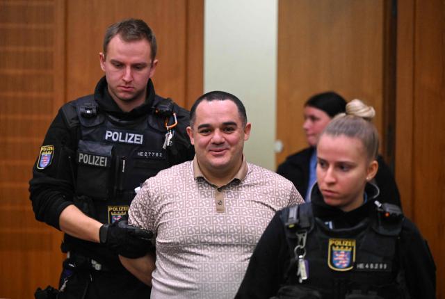 Co-defendant Ukrainian Robert A., is lead into the courtroom on the opening day of the trial of three men on charges of spying for Russia, in Frankfurt am Main, western Germany, on December 9, 2025. Three men go on trial in Germany on Tuesday, accused of tailing a former Ukrainian soldier on behalf of Russian intelligence services for a possible assassination plot. The alleged ringleader, an Armenian national partially identified as Vardges I., had recruited another Ukrainian, Robert A., and a Russian, Arman S., prosecutors charge. (Photo by POOL / AFP)