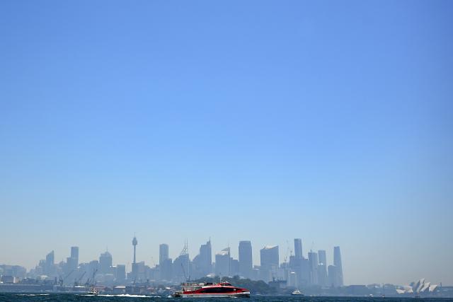 TOPSHOT - A passenger boat makes its way toward the harbour as smoke from bushfires burning on Sydney's outskirts hangs over Sydney Harbour on December 9, 2025. Dozens of bushfires burned along Australia's eastern seaboard on December 6, destroying several houses as a blistering heatwave set in. (Photo by SAEED KHAN / AFP)
