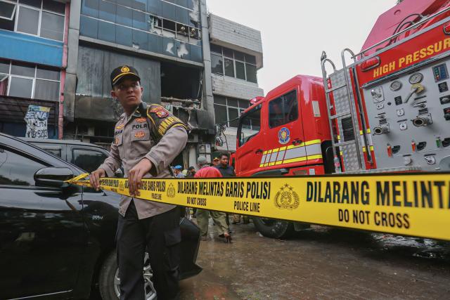 TOPSHOT - A member of the Indonesian police sets up a barricade tape to cordon off a seven-storey building where firefighters extinguished a fire that killed at least 20 people in central Jakarta on December 9, 2025. (Photo by SYNATRIA RESPATI / AFP)
