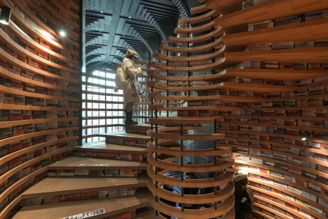 A woman stands on a spiral staircase at a bookstore in Tianjin on December 9, 2025. (Photo by ADEK BERRY / AFP)