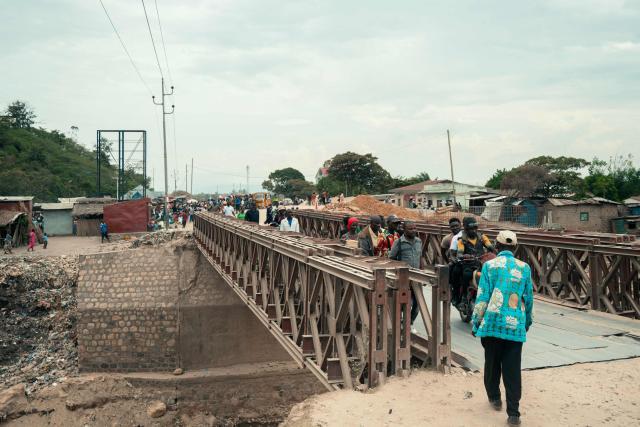 Commuters and pedestrians cross a bridge in Uvira on December 9, 2025. Intense fighting is taking place on Tuesday in the eastern Democratic Republic of Congo (DRC), with the M23 group, supported by the Rwandan army, continuing its rapid advance towards Uvira, a strategic Congolese city located near the border with neighboring Burundi and now under threat. The anti-government armed group and the Rwandan soldiers—estimated at 6,000 to 7,000 on Congolese soil according to UN experts—were reportedly only about fifteen kilometers north of the city, home to several hundred thousand inhabitants, as of Tuesday morning, according to security and military sources cited by AFP. (Photo by AFP)