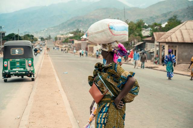 A woman balances a sack of flour on her head as she crosses a road in Uvira on December 9, 2025. Intense fighting is taking place on Tuesday in the eastern Democratic Republic of Congo (DRC), with the M23 group, supported by the Rwandan army, continuing its rapid advance towards Uvira, a strategic Congolese city located near the border with neighboring Burundi and now under threat. The anti-government armed group and the Rwandan soldiers—estimated at 6,000 to 7,000 on Congolese soil according to UN experts—were reportedly only about fifteen kilometers north of the city, home to several hundred thousand inhabitants, as of Tuesday morning, according to security and military sources cited by AFP. (Photo by AFP)