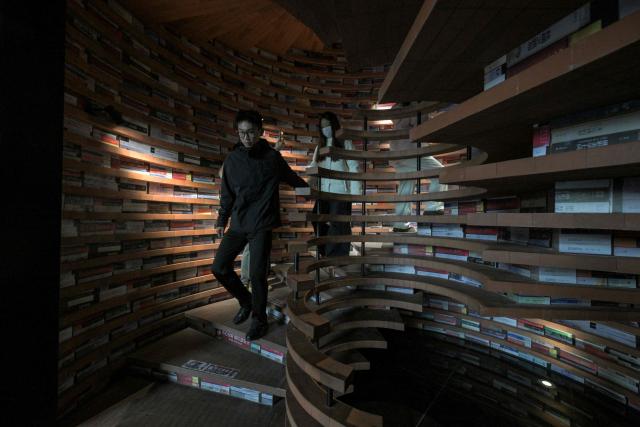 People climb down a spiral staircase at a bookstore in Tianjin on December 9, 2025. (Photo by ADEK BERRY / AFP)