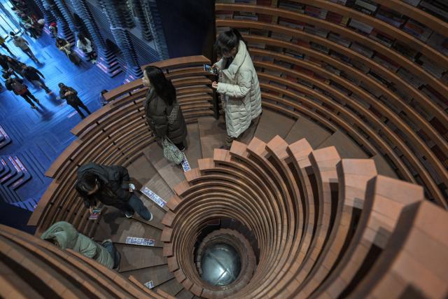 People climb down a spiral staircase at a bookstore in Tianjin on December 9, 2025. (Photo by ADEK BERRY / AFP)