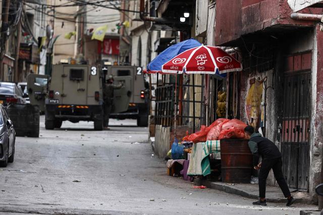 A young man looks at an Israeli soldier standing next to an army armoured vehicle during a military raid in Al-Amari refugee camp near the city of Ramallah in the Israeli-occupied West Bank on December 9, 2025. Violence in the West Bank, which Israel has occupied since 1967, has soared since the Hamas attack on Israel triggered the Gaza war in October 2023. At least 1,006 Palestinians, including militants, have been killed in the West Bank by Israeli forces or settlers since then, according to the Palestinian health ministry. During the same period, 43 Israelis, including soldiers, have been killed in Palestinian attacks in the West Bank, according to official Israeli figures. (Photo by Zain JAAFAR / AFP)