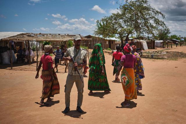 An armed Mozambican polics officer secures the are where internally displaced persons await the arrival of Vatican Secretary of State Cardinal PIetro Parolin at a centre in Naminawe, 30 km South West of Pemba, on December 9, 2025. Cardinal Parolin is in Mozambique to mark the 30th anniversary of diplomatic relations between the Holy See and the Southern African nation. Northern Mozambique has been battered by a bloody jihadist insurgency since late 2017. The group often referred to as "Al-Shabaab" by locals and authorities -- despite no known link to the Somali jihadist group -- seeks to impose Sharia law in Cabo Delgado, a neglected outpost that has become fertile ground for radical ideology. (Photo by Diego Menjíbar Reynés / AFP)