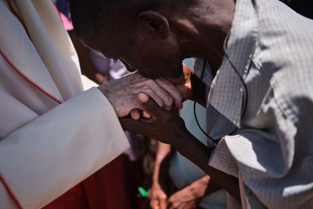 A man (R) kisses the hand of Vatican Secretary of State Cardinal PIetro Parolin as he meets displaced persons at a centre in Naminawe, 30 km South West of Pemba, on December 9, 2025. Cardinal Parolin is in Mozambique to mark the 30th anniversary of diplomatic relations between the Holy See and the Southern African nation. Northern Mozambique has been battered by a bloody jihadist insurgency since late 2017. The group often referred to as "Al-Shabaab" by locals and authorities -- despite no known link to the Somali jihadist group -- seeks to impose Sharia law in Cabo Delgado, a neglected outpost that has become fertile ground for radical ideology. (Photo by Diego Menjíbar Reynés / AFP)