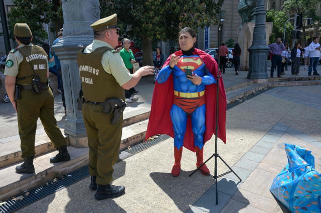 A Carabineros police officer asks for identification from a cosplayer dressed up as comic character Superman recording a video outside La Moneda Presidential Palace in Santiago on December 9, 2025. (Photo by Eitan ABRAMOVICH / AFP)