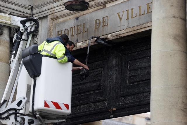 (FILES) City employees are at work in front of the burnt door of Bordeaux's city hall, on March 24, 2023, the day after it was set on fire by demonstrators during a rally against pension reform, a week after the government pushed a pensions reform through parliament without a vote, using the article 49.3 of the constitution. The new door of Bordeaux's city hall is set to be inaugurated on December 12, 2025, in the presence of Mayor Pierre Humic following its thirty-month restoration. (Photo by ROMAIN PERROCHEAU / AFP)