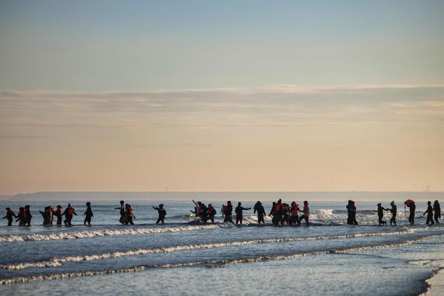 (FILES) Migrants wade into the sea to try to board smugglers' boats in an attempt to cross the English Channel off the beach of Gravelines, northern France on September 27, 2025. Prison sentences ranging from one to nine years were requested on December 9, 2025 against 17 suspected smugglers on trial since December 1 in Lille, accused of using "taxi boats" to illegally transport migrants to Britain in 2023. (Photo by Sameer Al-DOUMY / AFP)