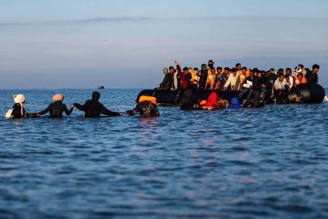 (FILES) Migrants wade into the sea to try to board smugglers' boats in an attempt to cross the English Channel off the beach of Gravelines, northern France on September 27, 2025. Prison sentences ranging from one to nine years were requested on December 9, 2025 against 17 suspected smugglers on trial since December 1 in Lille, accused of using "taxi boats" to illegally transport migrants to Britain in 2023. (Photo by Sameer Al-DOUMY / AFP)