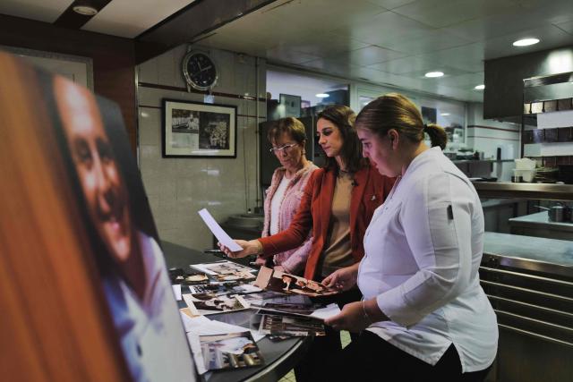 (FILES) Dominique Loiseau (L), wife of the late French chef Bernard Loiseau, and her daughters Berangere (C) and Blanche (R) flanked by a portrait of their late father (L), look at family photographs the kitchen of the restaurant "La Côte dOr - Le Relais Bernard Loiseau" in Saulieu, central France, on February 9, 2023. Dijon, Beaune, Besançon, Metz, and even Tokyo: despite the suicide of its eponymous owner, three-star chef Bernard Loiseau, in 2003, the establishment he founded 50 years ago has become a small empire. (Photo by Olivier CHASSIGNOLE / AFP)