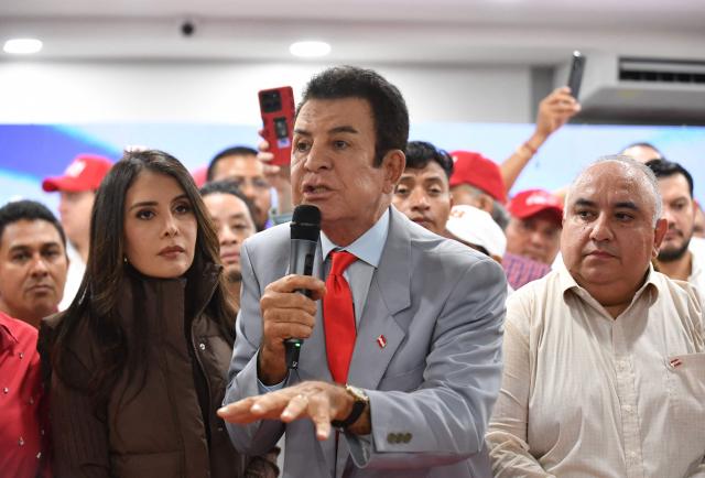 Salvador Nasralla, presidential candidate for the opposition Liberal Party, speaks during a press conference next to his wife Iroshka Elvir in Tegucigalpa on December 9, 2025. Nasralla made allegations of electoral corruption on December 9, 2025, after a stalled ballot count in the November 30 general election. (Photo by Orlando SIERRA / AFP)