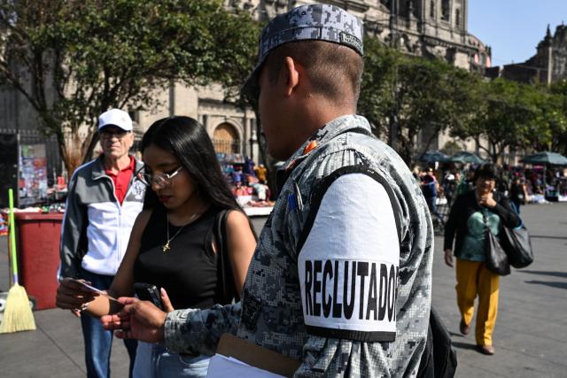 A member of the 14th Battalion "La Cofradia" of the Mexican National Guard distributes flyers with the requirements to join National Guard units in Jalisco during a voluntary recruitment campaign in Mexico City on December 9, 2025. (Photo by Yuri CORTEZ / AFP)
