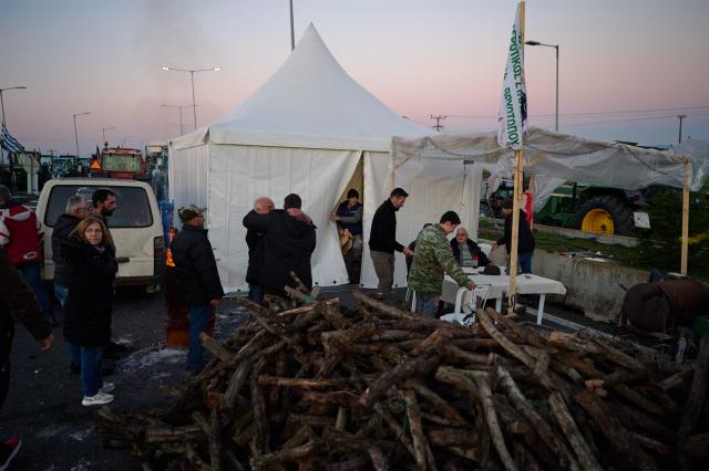 Farmers gather outside a makeshift tent as they block a national highway with their tractors  on the outskirts of the central Greek city of Larisa on December 9, 2025. Thousands of Greek farmers have since late November blocked highways, mainly in the centre and north of the country, to demand swifter access to EU subsidies delayed by an ongoing probe into multi-million fraud. (Photo by Aggelos NAKKAS / AFP)