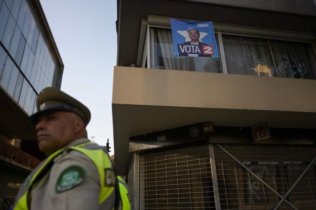 A Carabineros police officer patrols past a poster supporting Chilean presidential candidate Jeannette Jara of the Unidad por Chile coalition in Santiago on December 9, 2025. The second round of the Chilean presidential election on December 14, 2025, will pit two candidates who are totally opposed: Jeannette Jara, from a broad left-wing coalition with modest origins, and the far-right leader Jose Antonio Kast, an ultraconservative Catholic determined to massively expel undocumented migrants. (Photo by Eitan ABRAMOVICH / AFP)