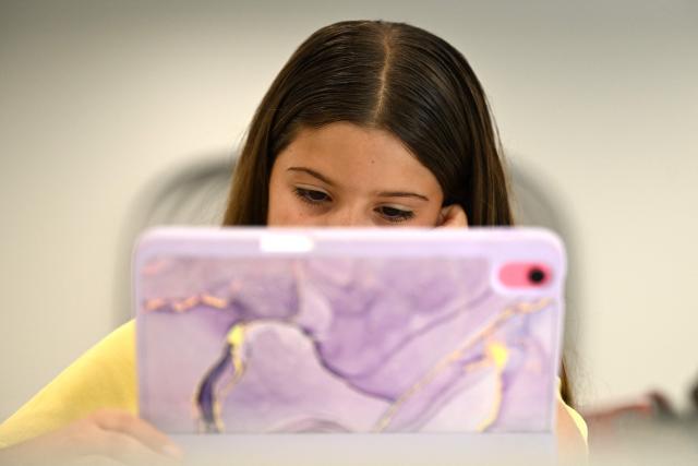 10-year-old Bianca Navarro browses through a list of cartoons youtube at her home in western Sydney on December 10, 2025. Australia banned young teenagers from social media on Wednesday, launching a world-first crackdown designed to unglue children from addictive scrolling on the likes of Facebook, Instagram and TikTok. (Photo by Saeed KHAN / AFP)
