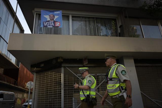 Carabineros police officers patrol past a poster supporting Chilean presidential candidate Jeannette Jara of the Unidad por Chile coalition in Santiago on December 9, 2025. The second round of the Chilean presidential election on December 14, 2025, will pit two candidates who are totally opposed: Jeannette Jara, from a broad left-wing coalition with modest origins, and the far-right leader Jose Antonio Kast, an ultraconservative Catholic determined to massively expel undocumented migrants. (Photo by Eitan ABRAMOVICH / AFP)