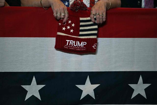 An attendee holds a hat with US President Donald Trump's name on it as he delivers remarks on the economy at Mount Airy Casino Resort in Mount Pocono, Pennsylvania, on December 9, 2025. (Photo by ANDREW CABALLERO-REYNOLDS / AFP)