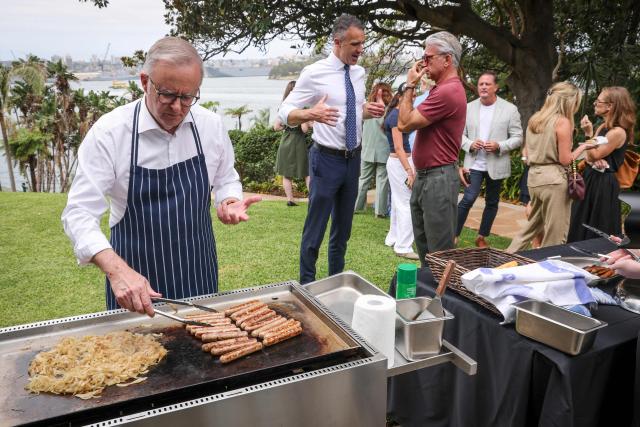 Australia’s Prime Minister Anthony Albanese (L) cooks sausages on a barbecue during an official function to mark the start of Australia’s social media reform at Kirrilbilli House in Sydney on December 10, 2025. Australia banned legions of young teenagers from social media with a world-first crackdown on December 10, declaring it was time to "take back control" from formidable tech giants. (Photo by DAVID GRAY / AFP)