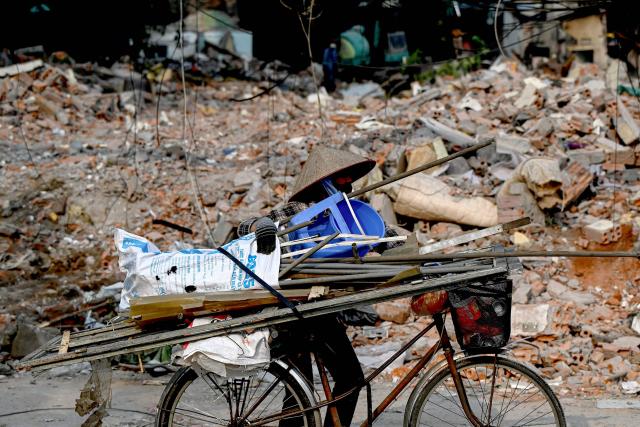 A woman pushes a bicycle loaded with scrap metal collected at a house demolition site in Hanoi on December 10, 2025. (Photo by Nhac NGUYEN / AFP)