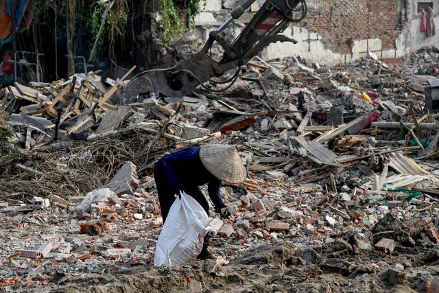 A woman collects scrap metal at a house demolition site in Hanoi on December 10, 2025. (Photo by Nhac NGUYEN / AFP)