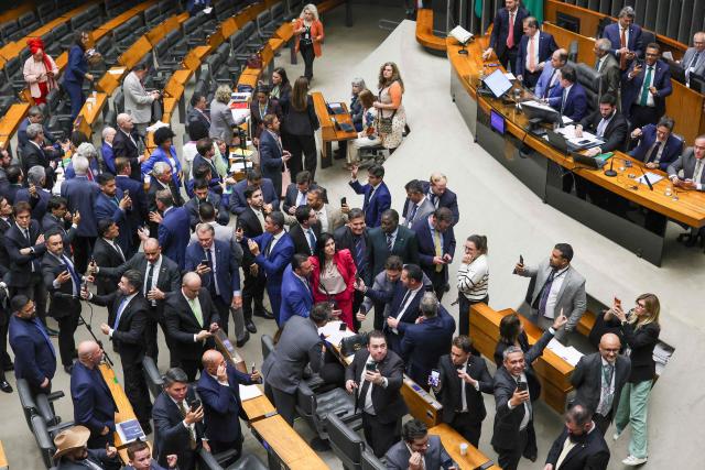 Lawmakers of Brazil's lower house of Congress celebrate after approving a bill that could slash former president Jair Bolsonaro's prison sentence for plotting a coup, in Brasilia on December 10, 2025. The far-right former leader has been serving a 27-year term since November after his conviction for a scheme to stop President Luiz Inacio Lula da Silva from taking office after the 2022 elections. (Photo by Sergio Lima / AFP)