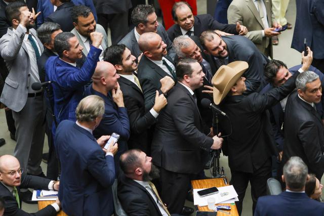 Lawmakers of Brazil's lower house of Congress celebrate after approving a bill that could slash former president Jair Bolsonaro's prison sentence for plotting a coup, in Brasilia on December 10, 2025. The far-right former leader has been serving a 27-year term since November after his conviction for a scheme to stop President Luiz Inacio Lula da Silva from taking office after the 2022 elections. (Photo by Sergio Lima / AFP)