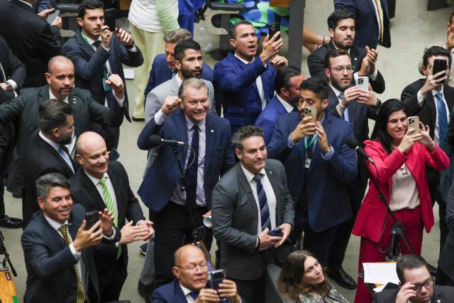 Lawmakers of Brazil's lower house of Congress celebrate after approving a bill that could slash former president Jair Bolsonaro's prison sentence for plotting a coup, in Brasilia on December 10, 2025. The far-right former leader has been serving a 27-year term since November after his conviction for a scheme to stop President Luiz Inacio Lula da Silva from taking office after the 2022 elections. (Photo by Sergio Lima / AFP)