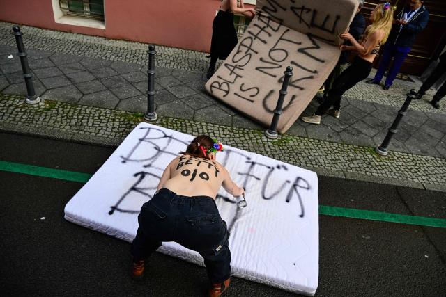 Topless members of the feminist activist group FEMEN spray slogans on mattresses during an action in support of jailed Moroccan activist Ibtissame "Betty" Lachgar on international Human Rights Day 2025, on December 10, 2025 in front of Morocco's embassy to Germany in Berlin. The 50-year-old clinical psychologist and feminist activist Ibtissame Lachgar was arrested in August 2025 after sparking an uproar for posting online a picture of herself wearing a T-shirt with the word "Allah" in Arabic followed by "is lesbian". A Moroccan court sentenced Lachgar to 30 months behind bars for "offending Islam". (Photo by John MACDOUGALL / AFP)
