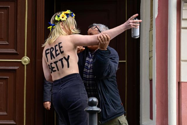 An embassy secuity guard tackles a topless members of the feminist activist group FEMEN as they spray slogans on mattresses during an action in support of jailed Moroccan activist Ibtissame "Betty" Lachgar on international Human Rights Day 2025, on December 10, 2025 in front of Morocco's embassy to Germany in Berlin. The 50-year-old clinical psychologist and feminist activist Ibtissame Lachgar was arrested in August 2025 after sparking an uproar for posting online a picture of herself wearing a T-shirt with the word "Allah" in Arabic followed by "is lesbian". A Moroccan court sentenced Lachgar to 30 months behind bars for "offending Islam". (Photo by John MACDOUGALL / AFP)