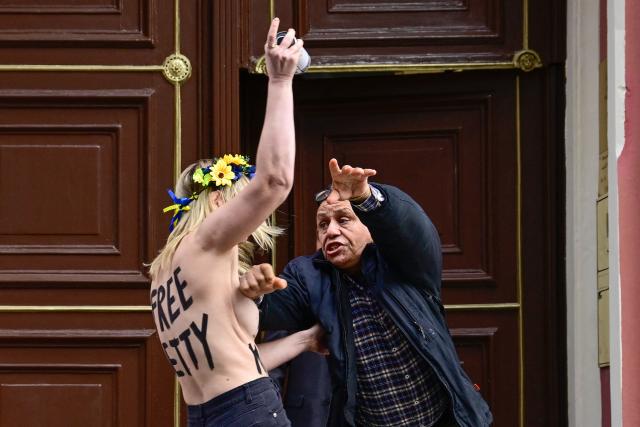 An embassy secuity guard tackles a topless members of the feminist activist group FEMEN as they spray slogans on mattresses during an action in support of jailed Moroccan activist Ibtissame "Betty" Lachgar on international Human Rights Day 2025, on December 10, 2025 in front of Morocco's embassy to Germany in Berlin. The 50-year-old clinical psychologist and feminist activist Ibtissame Lachgar was arrested in August 2025 after sparking an uproar for posting online a picture of herself wearing a T-shirt with the word "Allah" in Arabic followed by "is lesbian". A Moroccan court sentenced Lachgar to 30 months behind bars for "offending Islam". (Photo by John MACDOUGALL / AFP)