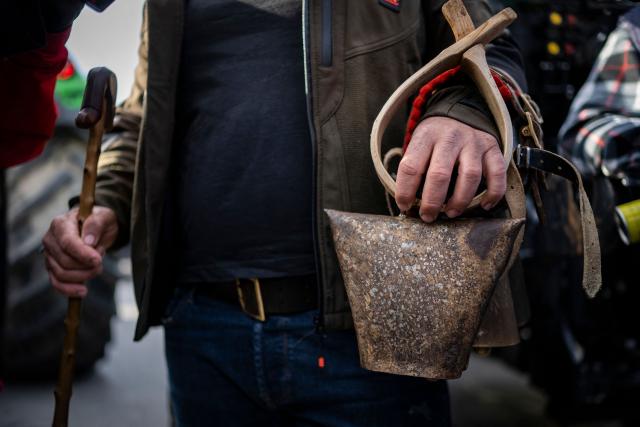 A farmer holds a cowbell as farmers take part in the blocking of the passengers' port of the central Greek city of Volos during a demonstration on December 10, 2025. Thousands of Greek farmers have since late November 2025 blocked highways, mainly in the centre and north of the country, to demand swifter access to EU subsidies delayed by an ongoing probe into multi-million fraud. (Photo by Aris MESSINIS / AFP)