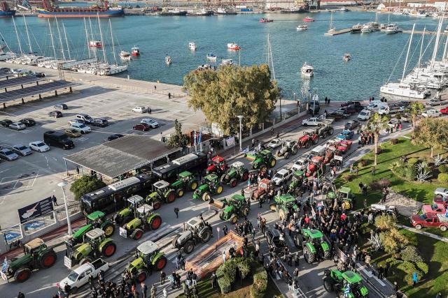 This aerial photograph shows farmers gathered as they take part in the blocking of the passengers' port of the central Greek city of Volos during a demonstration on December 10, 2025. Thousands of Greek farmers have since late November 2025 blocked highways, mainly in the centre and north of the country, to demand swifter access to EU subsidies delayed by an ongoing probe into multi-million fraud. (Photo by Aris MESSINIS / AFP)