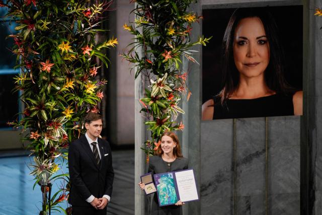 Ana Corina Sosa (R), daughter of Venezuelan opposition leader Maria Corina Machado, receives the Nobel Peace Prize for her mother (on the photo) from the Chair of the Norwegian Nobel Committee Jorgen Watne Frydnes (L) at the Nobel Peace Prize ceremony at Oslo City Hall on December 10, 2025 in Oslo, Norway. The 2025 Nobel Peace Prize was awarded to Machado for her efforts to bring democracy to Venezuela, challenging the iron-fisted rule of Venezuelan President Nicolas Maduro, who has been president since 2013. (Photo by Stian Lysberg Solum / NTB / AFP) / Norway OUT