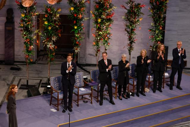 Ana Corina Sosa (L), daughter of Venezuelan opposition leader Maria Corina Machado, receives a standing ovation from the audience including Norwegian Nobel Committee  members Chair Jorgen Watne Frydnes (L-R), Asle Toje, Anne Enger, Kristin Clemet, Gry Larsen and Kristian Berg Harpviken following her speach after receiving the Nobel Peace Prize for her mother at the Nobel Peace Prize ceremony at Oslo City Hall on December 10, 2025 in Oslo, Norway. The 2025 Nobel Peace Prize was awarded to Machado for her efforts to bring democracy to Venezuela, challenging the iron-fisted rule of Venezuelan President Nicolas Maduro, who has been president since 2013. (Photo by Odd ANDERSEN / AFP)