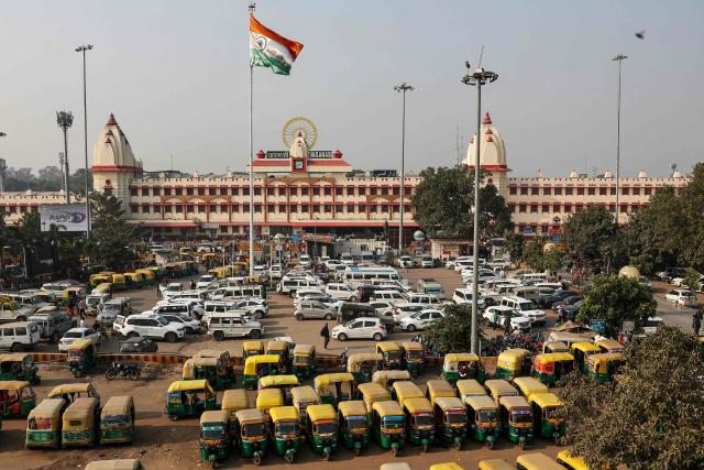India's national flag flutters as auto rickshaws and vehicles lie parked at a railway station in Varanasi on December 10, 2025. (Photo by Niharika KULKARNI / AFP)