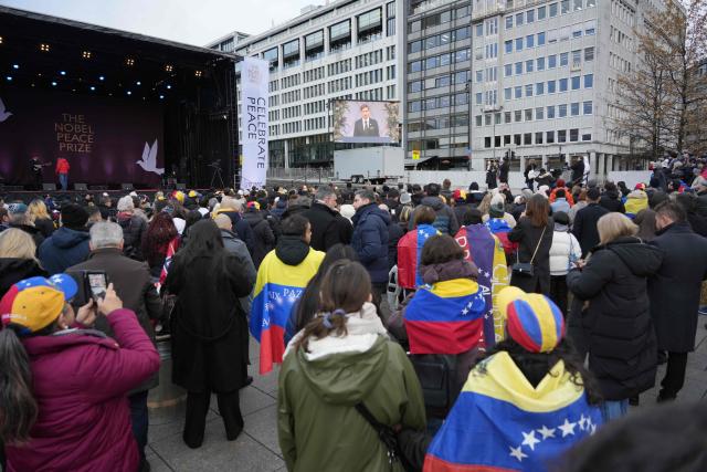 Spectators wearing Venezuelan flags and hats follow the 2025 Nobel Peace Prize ceremony on a screen installed outside at Radhusplassen in Oslo on December 10, 2025. The 2025 Nobel Peace Prize was awarded to Maria Corina Machado for her efforts to bring democracy to Venezuela, challenging the iron-fisted rule of Venezuelan President Nicolas Maduro, who has been president since 2013. (Photo by Gorm Kallestad / NTB / AFP) / Norway OUT