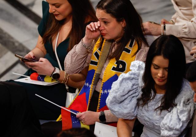 Guests holding Venezuelan flags and wearing a Venezuelan scarf attend the 2025 Nobel Peace Prize ceremony at Oslo City Hall on December 10, 2025 in Oslo, Norway. The 2025 Nobel Peace Prize was awarded to Maria Corina Machado for her efforts to bring democracy to Venezuela, challenging the iron-fisted rule of Venezuelan President Nicolas Maduro, who has been president since 2013. (Photo by Odd ANDERSEN / AFP)