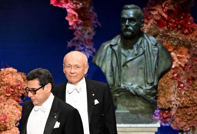Laureate of The Sveriges Riksbank Prize in Economic Sciences 2025 French economist Philippe Aghion (L) and laureate of The Sveriges Riksbank Prize in Economic Sciences 2025 Canadian economist Peter Howitt walk past a bust of Alfred Nobel as they arrive to attend the Nobel Prize award ceremony on December 10, 2025 in Stockholm, Sweden. The laureates will receive their prizes at formal ceremonies in Stockholm and Oslo on December 10. That date is the anniversary of the death in 1896 of scientist Alfred Nobel, who created the prizes in his will. (Photo by Jonathan Nackstrand / AFP)