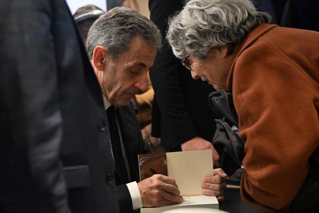 France's former President Nicolas Sarkozy signs a copy of his book "Diary of a Prisoner" for a reader on the day of its release at the Lamartine bookshop in Paris on December 10, 2025. Sarkozy has written a 216-page book entitled "Diary of a Prisoner," released on December 10, 2025 and excerpts of which were published in several French media on December 6, 2025. Nicolas Sarkozy, who was president from 2007 to 2012, was protected in prison by two security officers and remained confined to his cell 23 hours a day, except for visiting hours. (Photo by Bertrand GUAY / AFP)