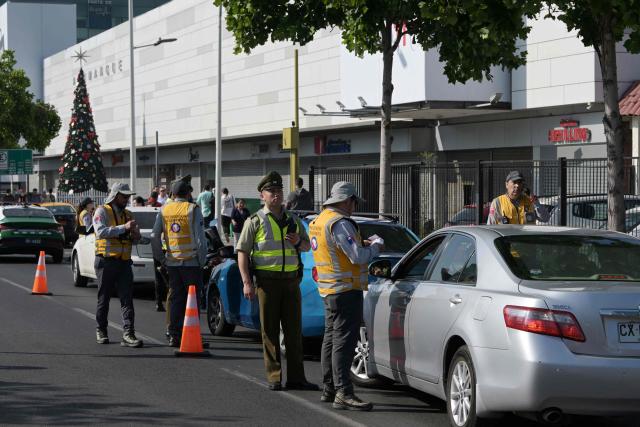 A police officer checks the ID of a driver during a joint operation with private security from Las Condes municipality in Santiago on December 10, 2025. The second round of the Chilean presidential election on December 14 will pit two candidates against each other who are diametrically opposed: Jeannette Jara, the representative of a broad left-wing coalition with modest origins, and the far-right leader Jose Antonio Kast, an ultraconservative Catholic determined to massively expel undocumented migrants. (Photo by Rodrigo ARANGUA / AFP)