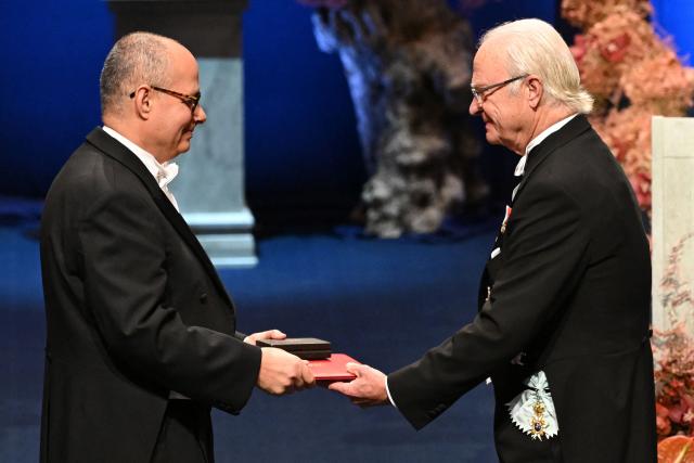 King Carl XVI Gustaf of Sweden (R) hands over the award to Nobel Prize in Chemistry 2025 laureate US-Jordanian chemist Omar M. Yaghi during the award ceremony on December 10, 2025 in Stockholm, Sweden. The laureates received their prizes at formal ceremonies in Stockholm and Oslo on December 10. That date is the anniversary of the death in 1896 of scientist Alfred Nobel, who created the prizes in his will. (Photo by Jonathan Nackstrand / AFP)
