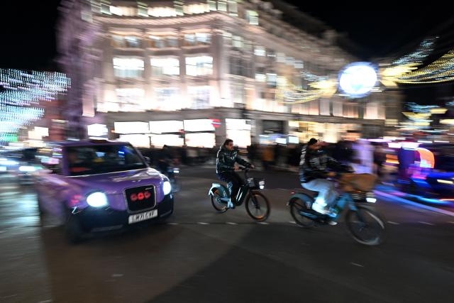 People ride electric e-bikes alongside a taxi, under the annual Christmas lights on Oxford Street, in central London, on December 10, 2025. (Photo by JUSTIN TALLIS / AFP)