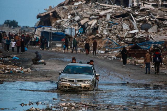 A man drives a car through a pool of watervin the Al-Saftawi neighborhood, west of Jabalia city in the northern Gaza Strip on December 10, 2025. (Photo by BASHAR TALEB / AFP)
