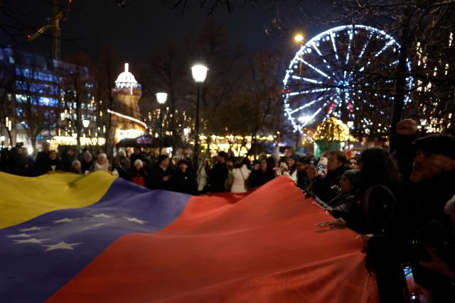 People hold a Venezualian flag as they take part in a torchlight procession organized by The Norwegian Venezuelan Justice Alliance in honor of Nobel Peace Prize laureate Maria Corina Machado in Oslo, Norway, on December 10, 2025. The daughter of the Nobel Peace Prize laureate, Ana Corina Sosa, accepted the award on behalf of her mother during a ceremony at Oslo City Hall. Venezuelan opposition leader Maria Corina Machado received the award for her tireless work to secure democratic rights for the people of Venezuela, and for her fight for a just and peaceful transition from dictatorship to popular rule. Due to the circumstances in her home country of Venezuela, the Nobel Peace Prize laureate was unable to attend the award ceremony in Norway. (Photo by Odd ANDERSEN / AFP) / Norway OUT
